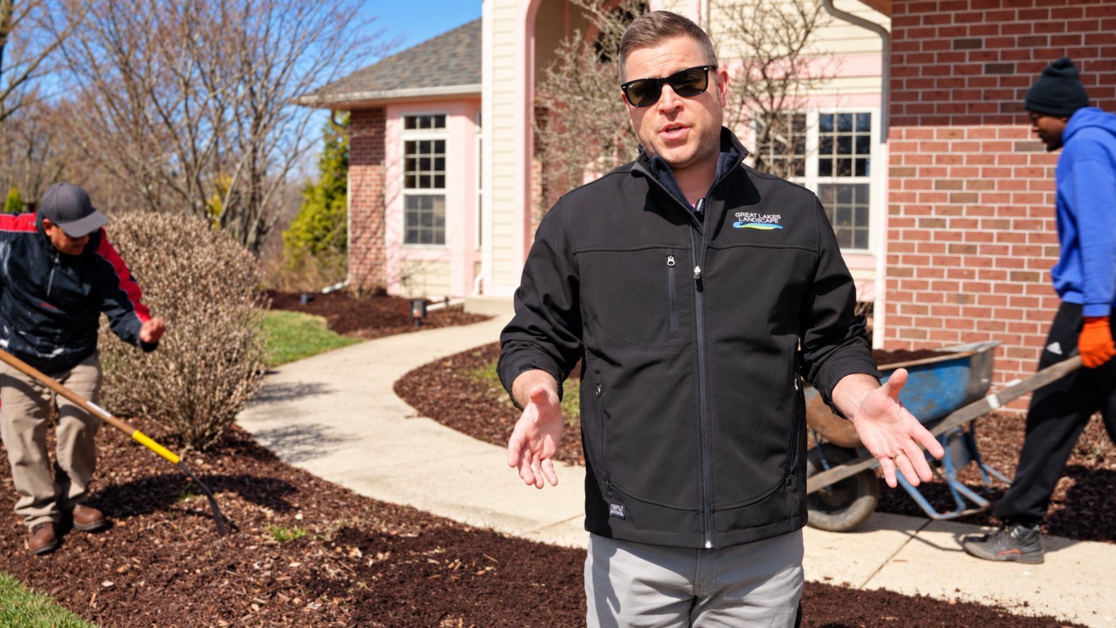 Landscape company owner talking on camera while his crew works behind him